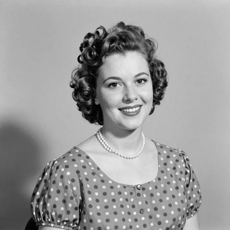 A 1952 black and white studio portrait of a young woman with curled hair and pearls