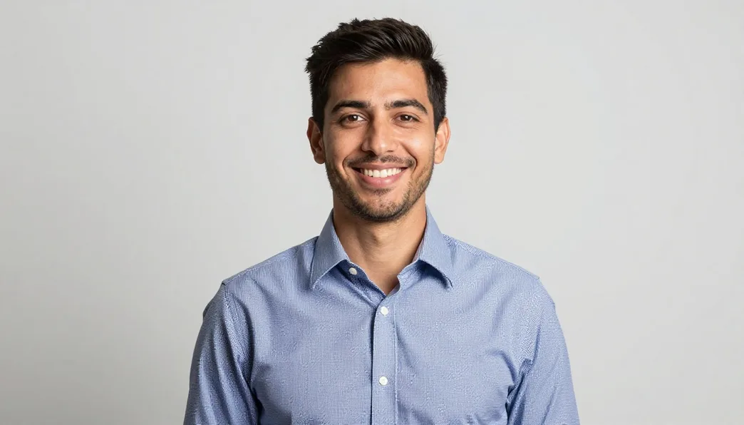 A smiling man in a blue shirt against a neutral grey studio background.